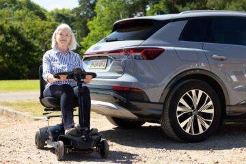 Lady smiling whilst sat on her mobility scooter in front of her Audi Q4 E-Tron