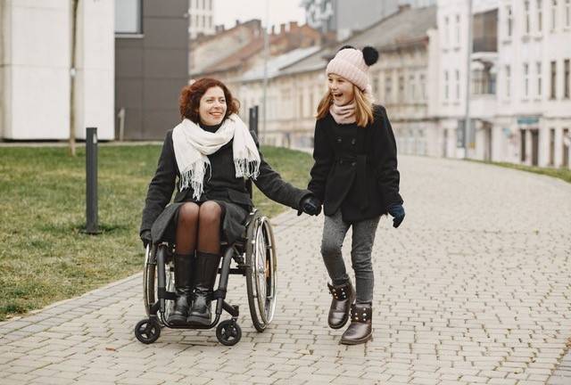 Accessible Attractions in UK blog - Mother in wheelchair smiling and holding hands with young daughter.