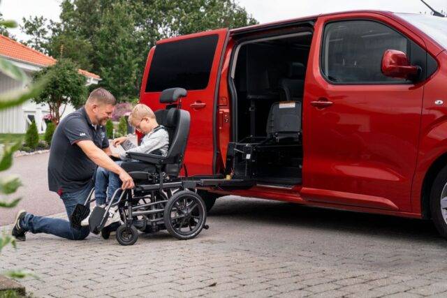 Young boy in wheelchair smiling with dad who is sliding the chair onto the swivel seat base in their car - choosing the right vehicle for your family